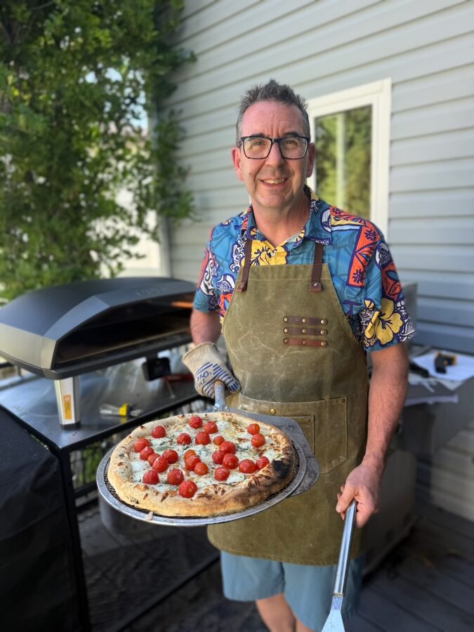 Troy Cox holding a freshly baked homemade pizza from his outdoor pizza oven