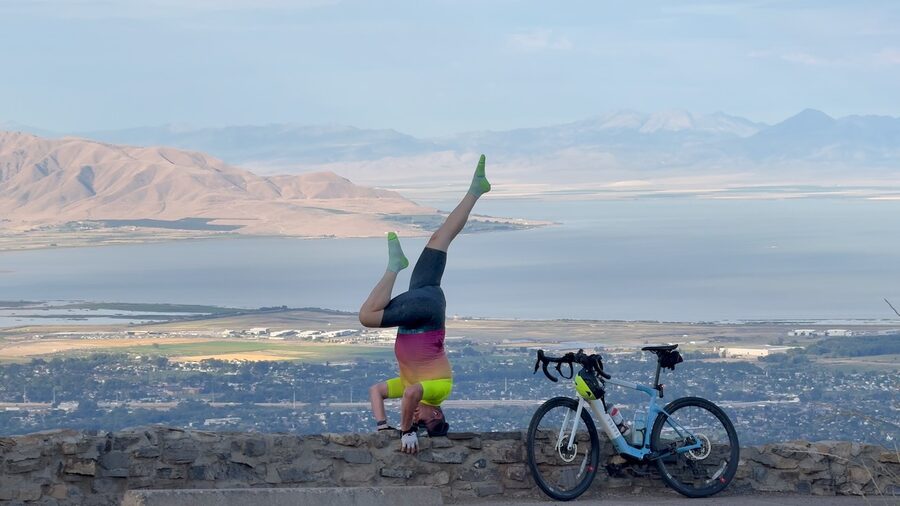 Troy Cox doing a yoga headstand on a stone wall overlooking Utah Lake, next to his gravel bike
