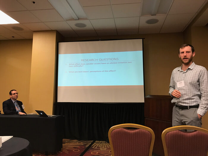 Jacob Barrows presenting his thesis research at a conference, with Troy Cox seated nearby